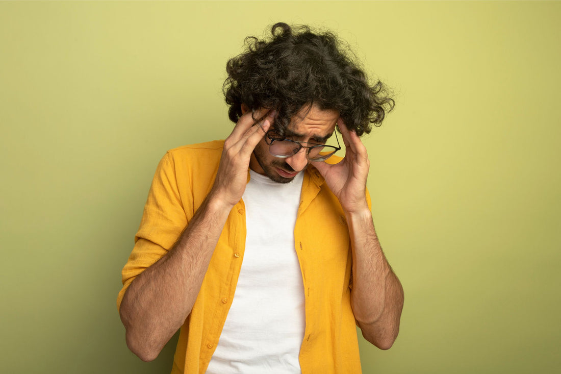 Aching young handsome caucasian man wearing glasses putting hands on head looking down suffering from headache isolated on olive green wall with copy space